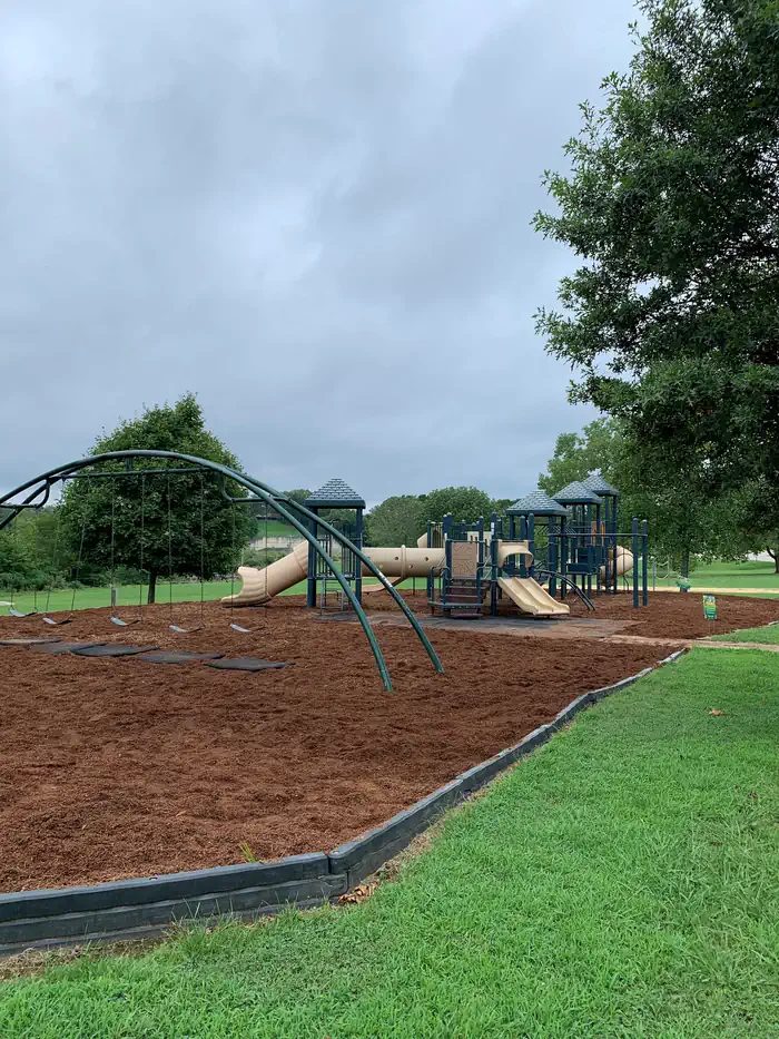 This playground area is near a volleyball court and corn hole set