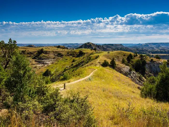 A hiking trail winds along a grass-covered ridge under a deep blue sky