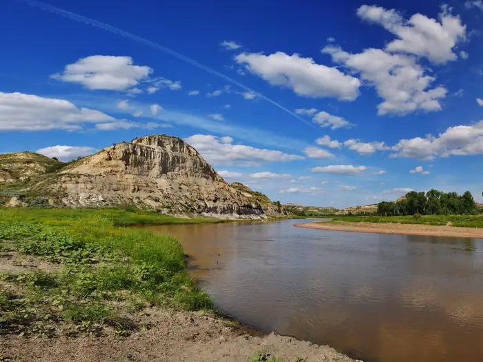 The Little Missouri River under a deep blue sky with a dramatic butte in the background