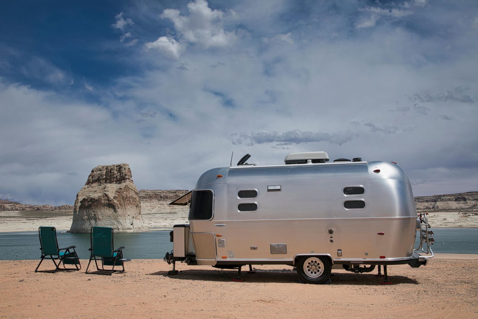 An Airstream and beach chairs on the shore at Lone Rock Beach, with Lake Powell and sandstone cliffs