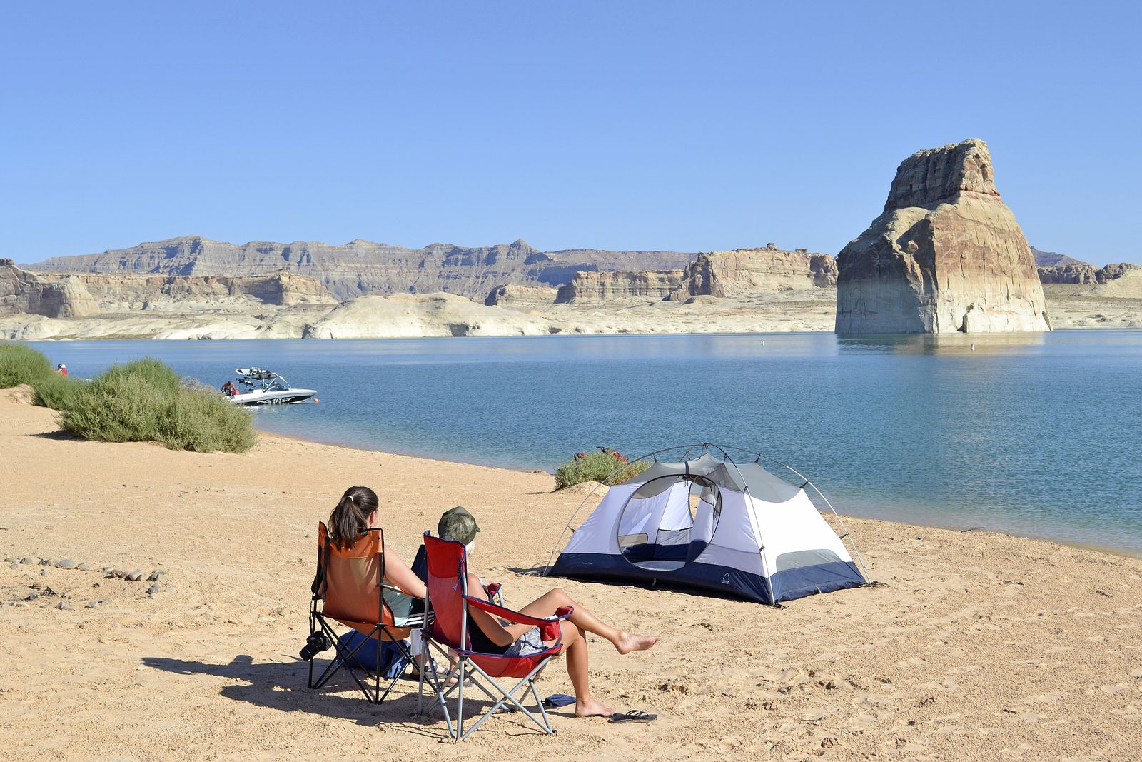 Two campers in beach chairs beside a tent at the water line on Lone Rock Beach