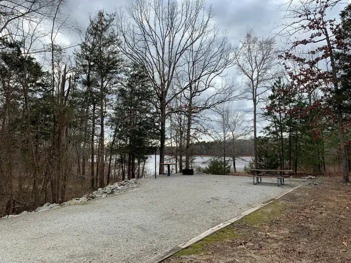 This is a photo of site 6. Most campsites are graveled. This site has a picnic table, utility table, lantern post and a fire ring/grill